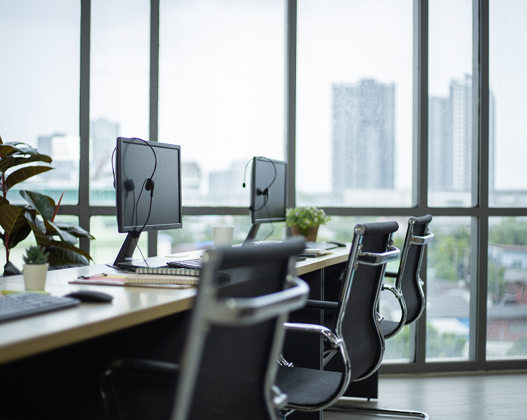 Postazioni di lavoro in un ufficio moderno e luminoso, con monitor, cuffie, sedie da ufficio e ampie vetrate - Fondo Sanità TLC